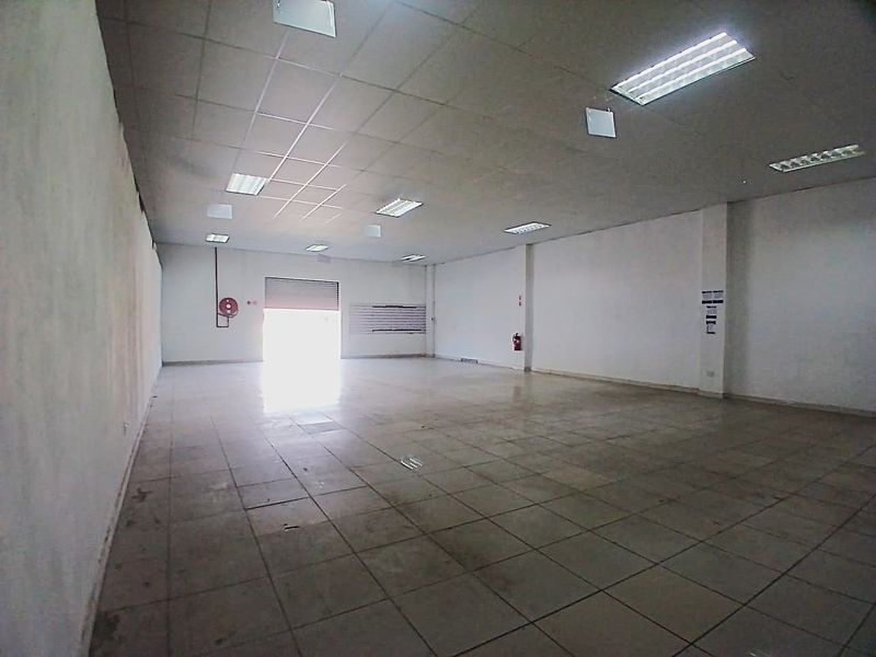 Spacious open-plan retail unit featuring tiled flooring, suspended ceilings with recessed lighting, and a rear roller shutter door for convenient access.