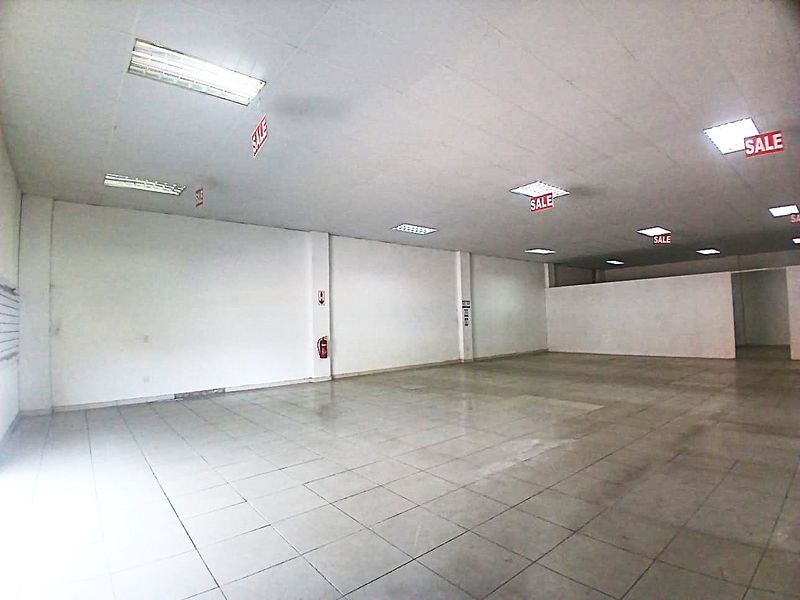 A spacious, empty open-plan retail unit featuring tiled flooring and recessed ceiling lighting, suitable for various commercial business applications.