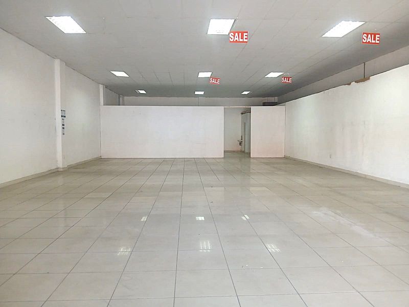 Spacious open-plan retail area featuring ceramic floor tiles, a suspended ceiling with recessed lighting, and a neutral white finish throughout.