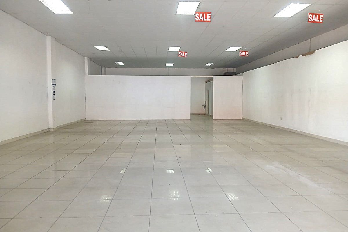 Spacious open-plan retail area featuring ceramic floor tiles, a suspended ceiling with recessed lighting, and a neutral white finish throughout.
