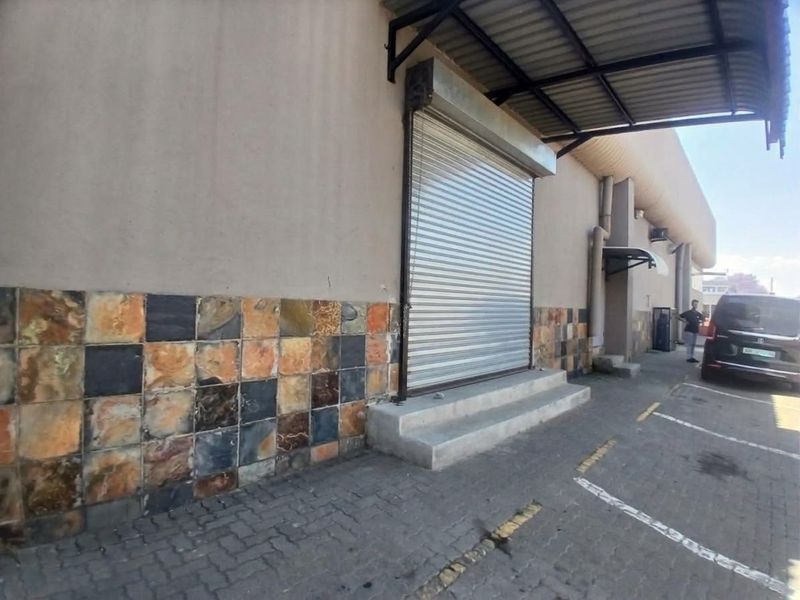Exterior view of a retail unit featuring a roller shutter door, metal awning, and decorative stone tile cladding with adjacent paved parking.