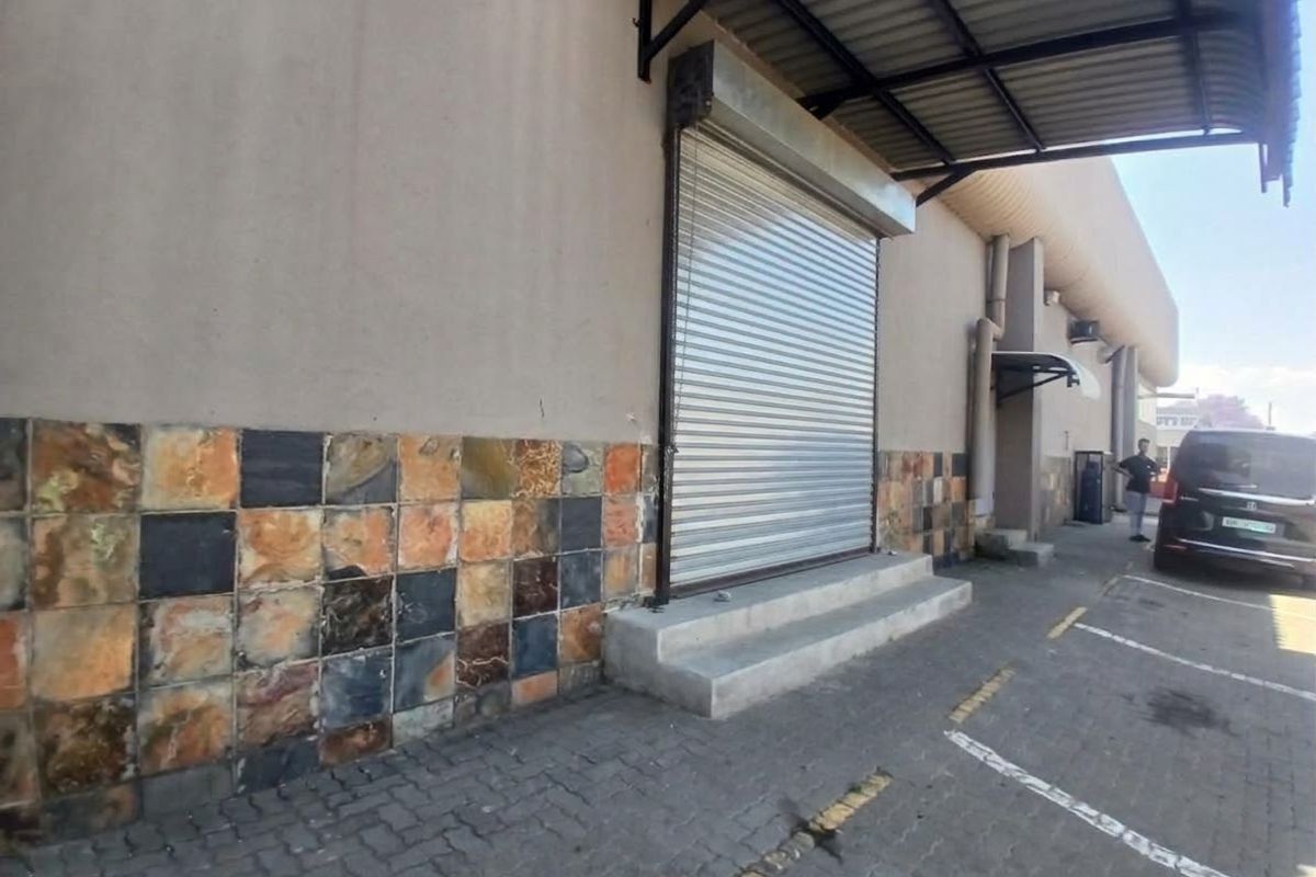Exterior view of a retail unit featuring a roller shutter door, metal awning, and decorative stone tile cladding with adjacent paved parking.