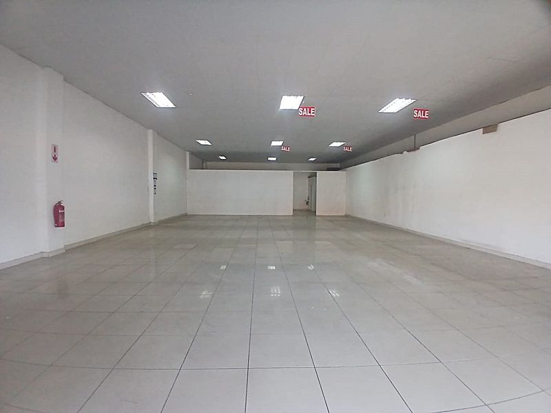 A spacious, empty retail unit featuring tiled flooring, a suspended ceiling with recessed lighting, and neutral white walls, ready for custom fit-out.