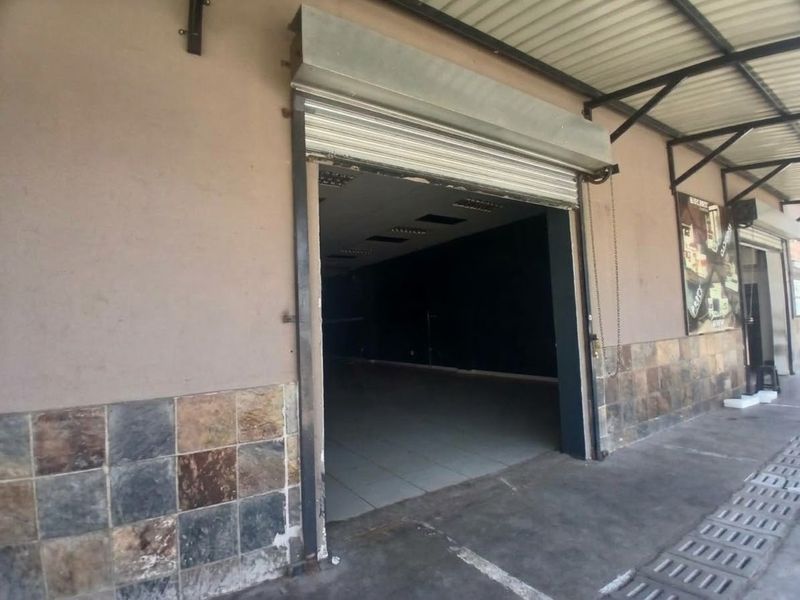 Front exterior view of a retail unit featuring a roller shutter door, tiled facade cladding, and a covered walkway area.