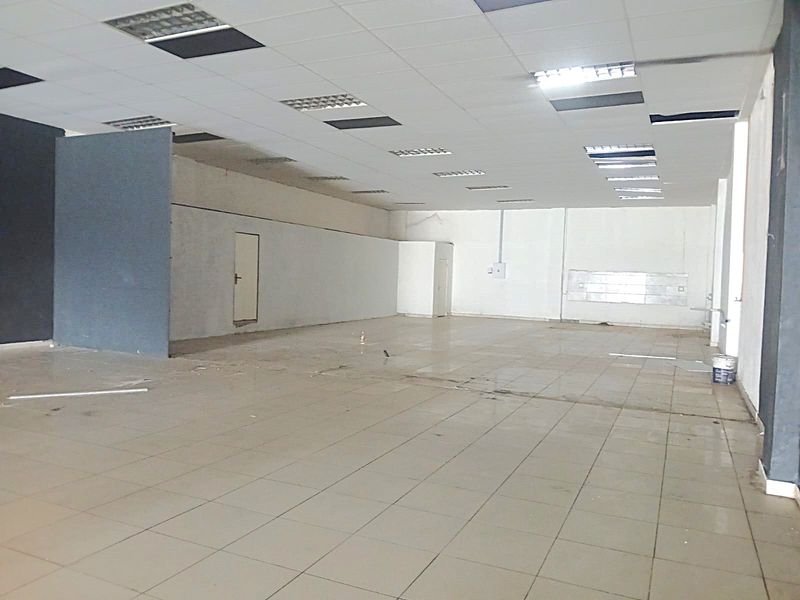 Spacious open-plan retail area featuring tiled flooring, a suspended ceiling with recessed lighting, and a partition wall, currently in need of cosmetic refurbishment.