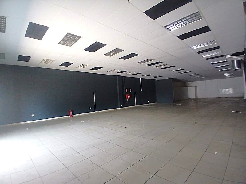 Spacious open-plan retail area featuring tiled flooring, a suspended ceiling with recessed lighting, and essential fire safety equipment.