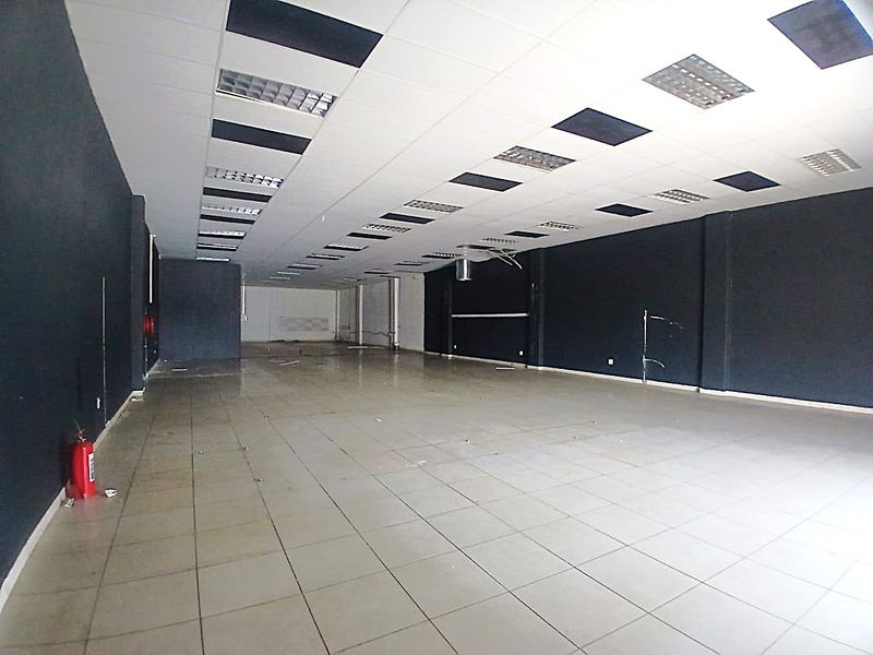 A spacious, empty retail unit featuring tiled flooring, a suspended ceiling with recessed lighting, and dark-painted walls, suitable for various commercial business applications.