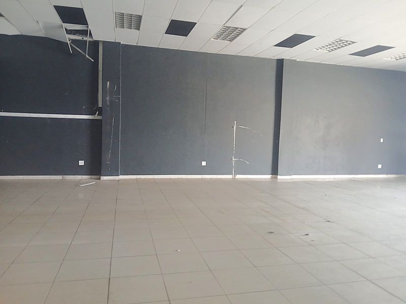 An empty open-plan retail space featuring tiled flooring, a suspended ceiling with recessed lighting, and dark grey painted walls requiring maintenance.