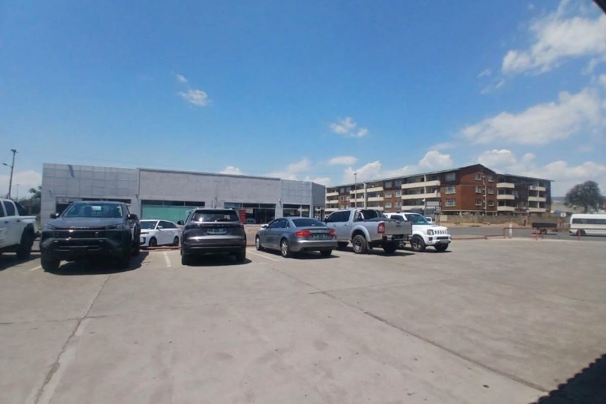 Exterior view of a retail property featuring a large concrete parking area and a commercial building facade with glass storefront windows.
