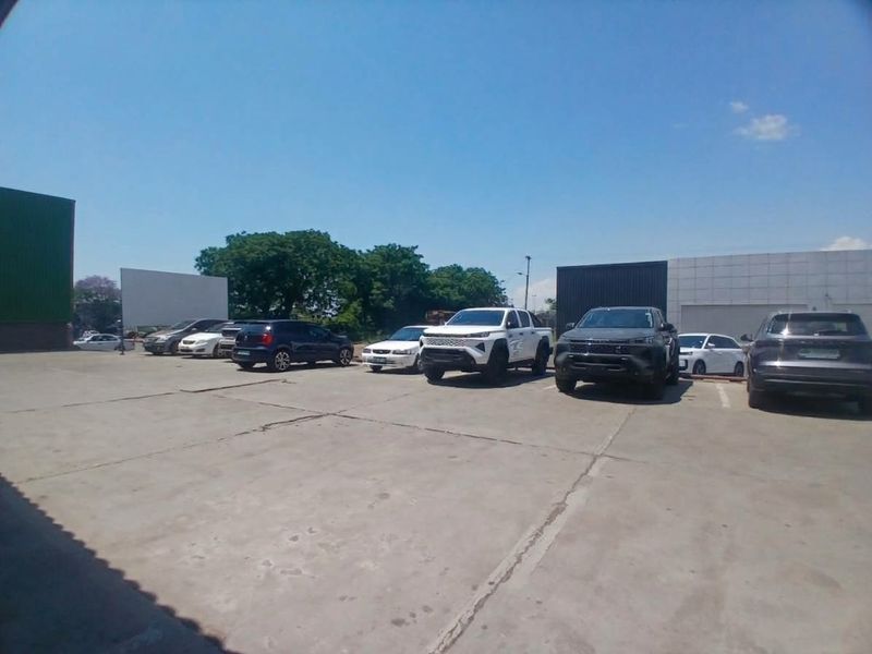 An exterior view of a commercial property featuring a large concrete parking area and industrial building facades.