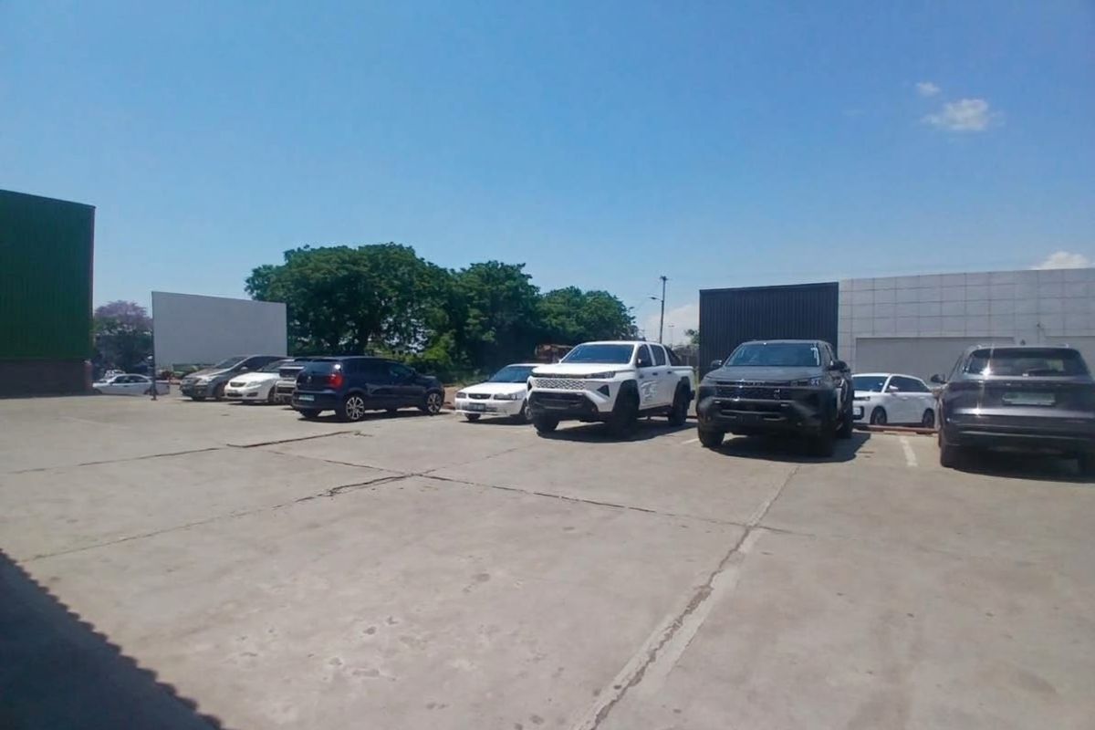 An exterior view of a commercial property featuring a large concrete parking area and industrial building facades.