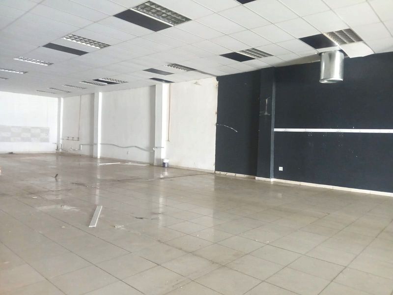 An empty open-plan retail space featuring ceramic tile flooring, a suspended ceiling with recessed lighting, and an exposed ventilation duct.