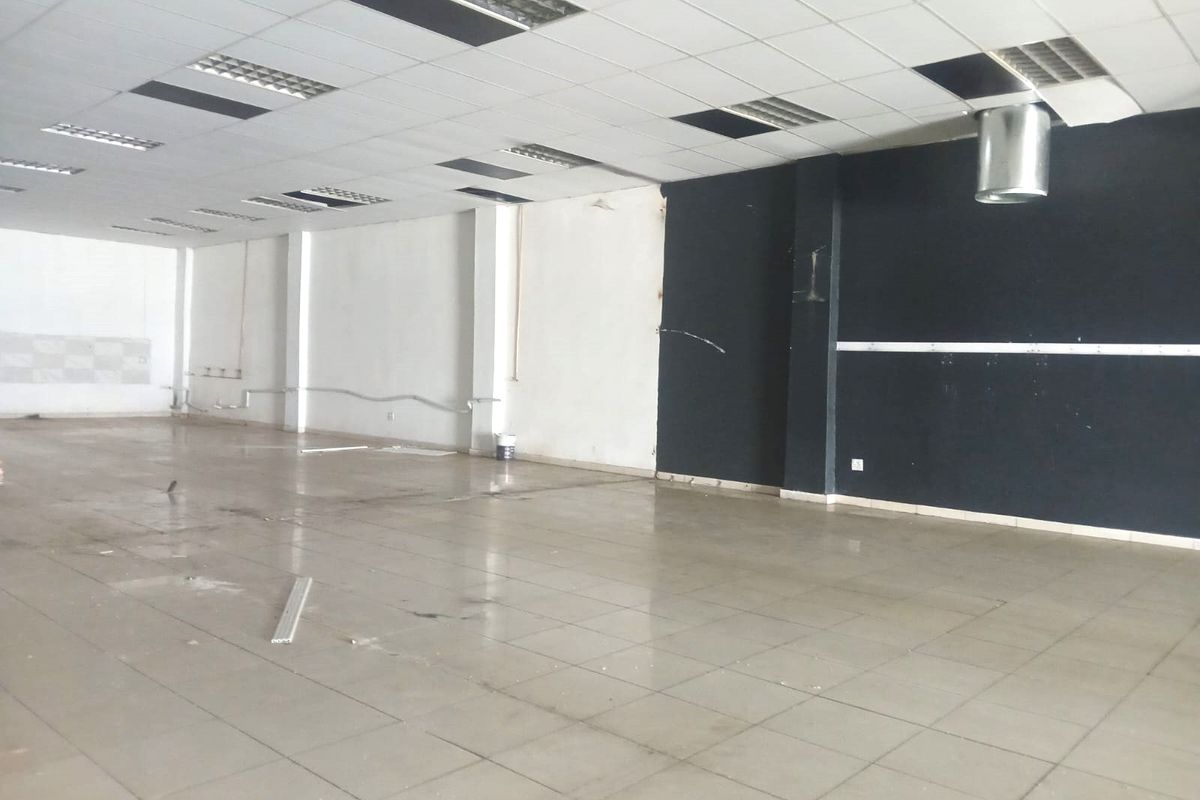 An empty open-plan retail space featuring ceramic tile flooring, a suspended ceiling with recessed lighting, and an exposed ventilation duct.