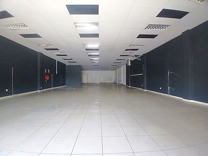 A spacious, empty retail unit featuring ceramic tiled flooring, a suspended ceiling with recessed lighting, and dark painted walls.