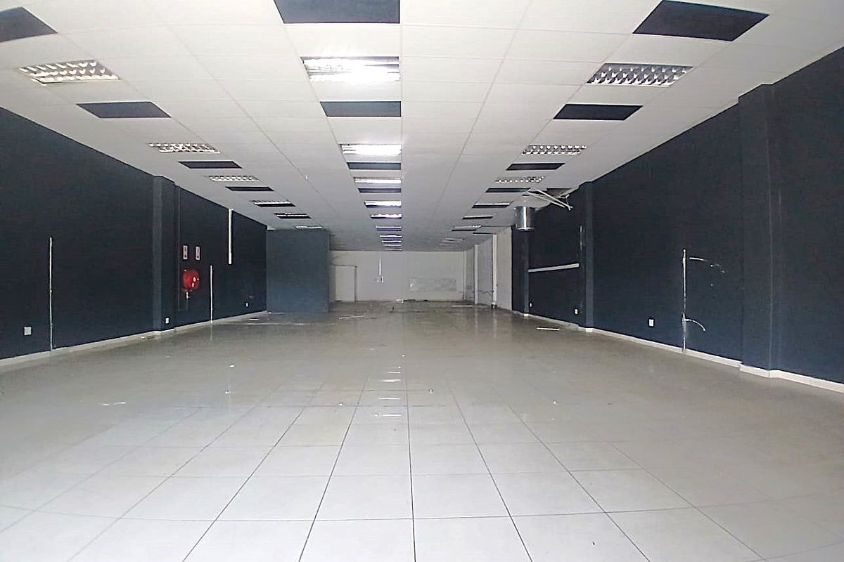 A spacious, empty retail unit featuring ceramic tiled flooring, a suspended ceiling with recessed lighting, and dark painted walls.
