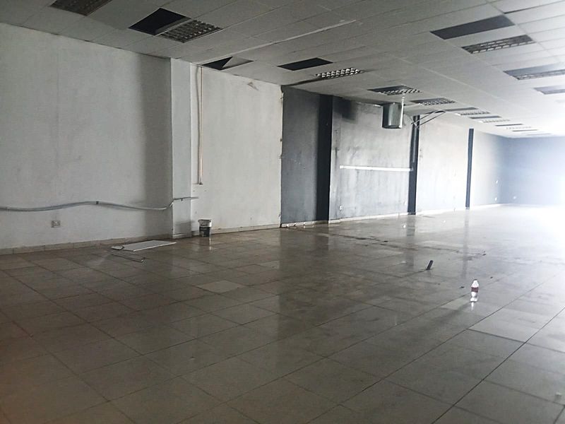 A large, vacant open-plan retail space featuring tiled flooring, a suspended ceiling with recessed lighting, and exposed ducting, ready for custom fit-out.