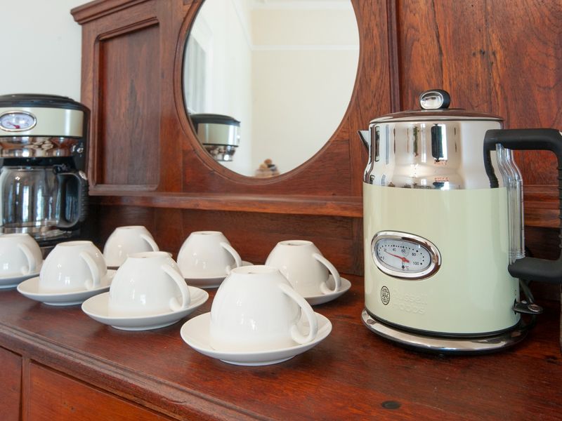 A close-up view of a vintage-style wooden sideboard featuring a built-in mirror, displaying a coffee maker and kettle with matching tea service.
