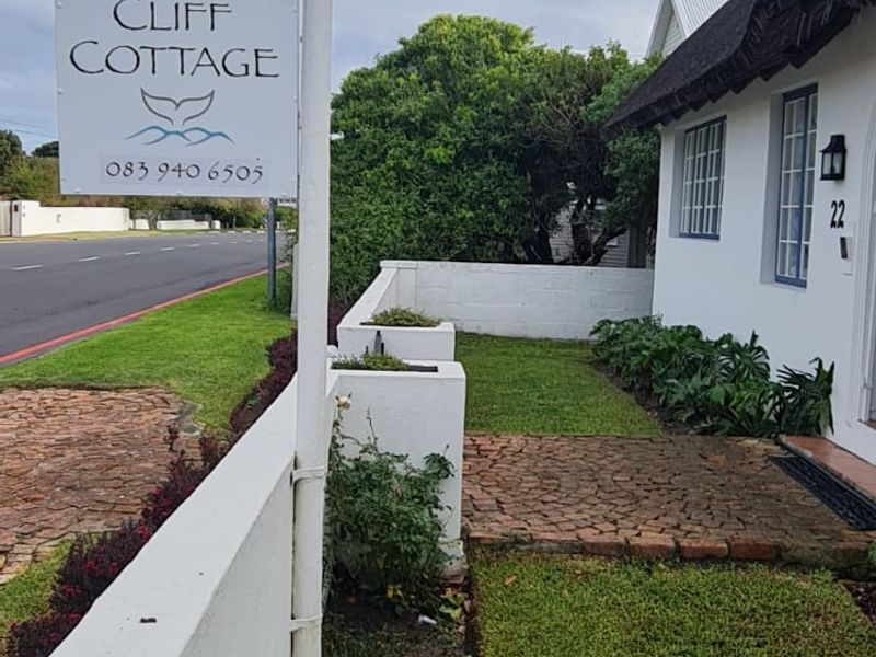 Front exterior view of Cliff Cottage featuring a charming thatched roof, well-maintained garden, and a brick-paved entrance path.
