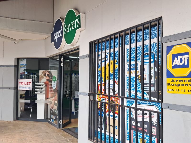 Front facade of a retail unit featuring a glass storefront, security gate, and prominent signage in a commercial shopping center.