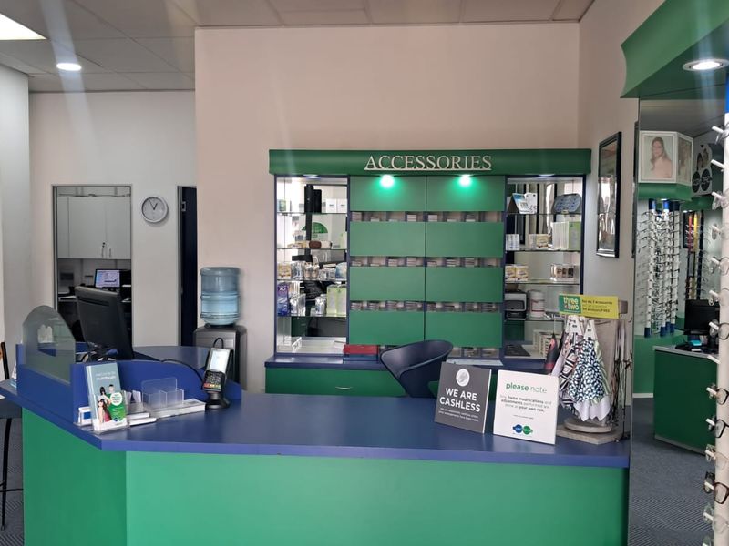 A retail optometry reception area featuring a built-in service counter, integrated display shelving for accessories, and professional recessed lighting.