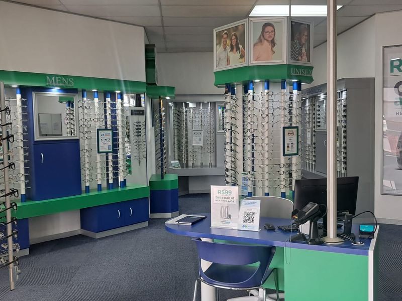A retail optometry store interior featuring custom built-in display shelving units, a central service counter, and professional retail lighting.
