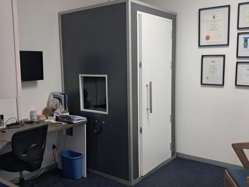 Professional office space featuring a built-in soundproof booth, fitted desk, and carpeted flooring, suitable for clinical or private consultation use.