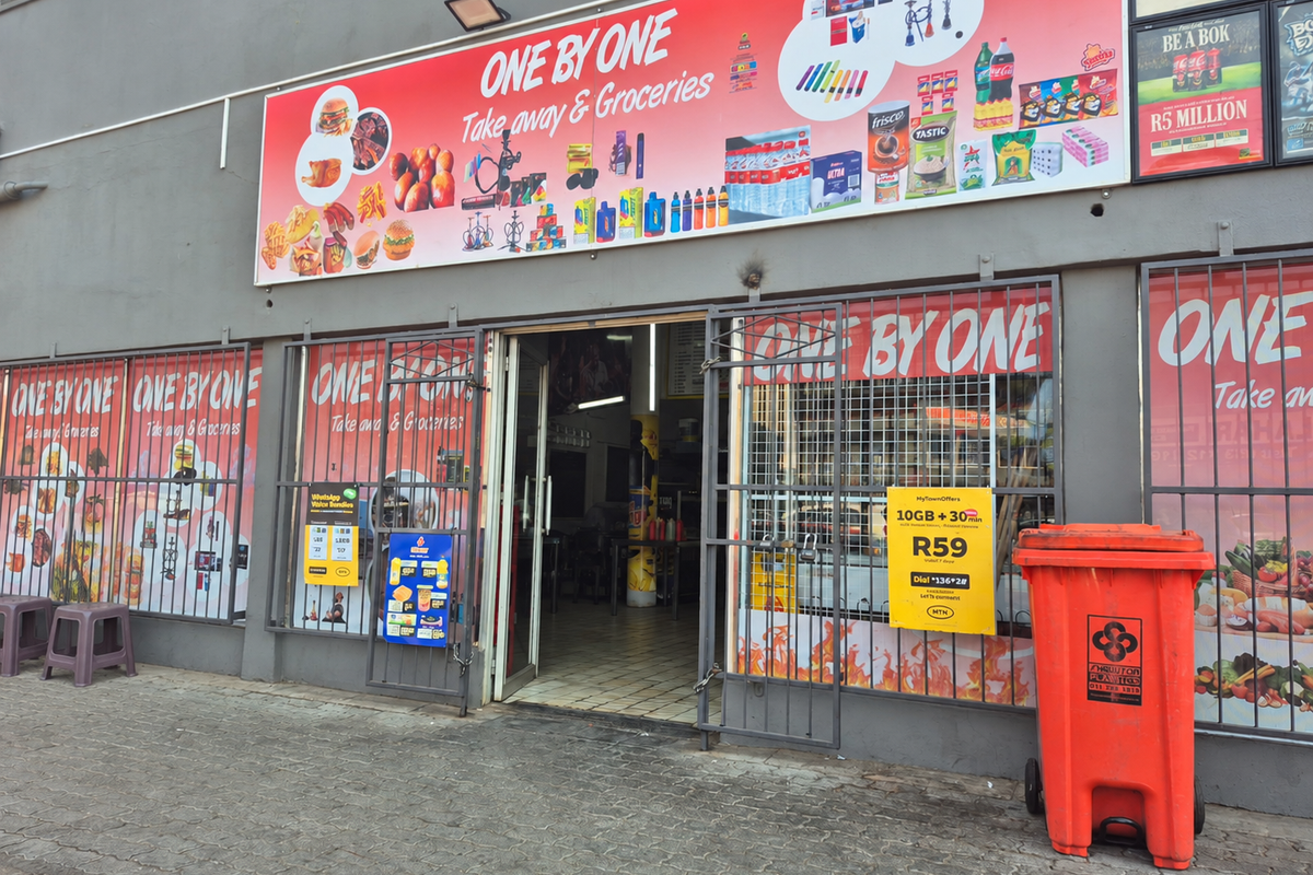 Commercial storefront entrance featuring prominent signage, security gates, and tiled flooring, suitable for a takeaway and grocery business.