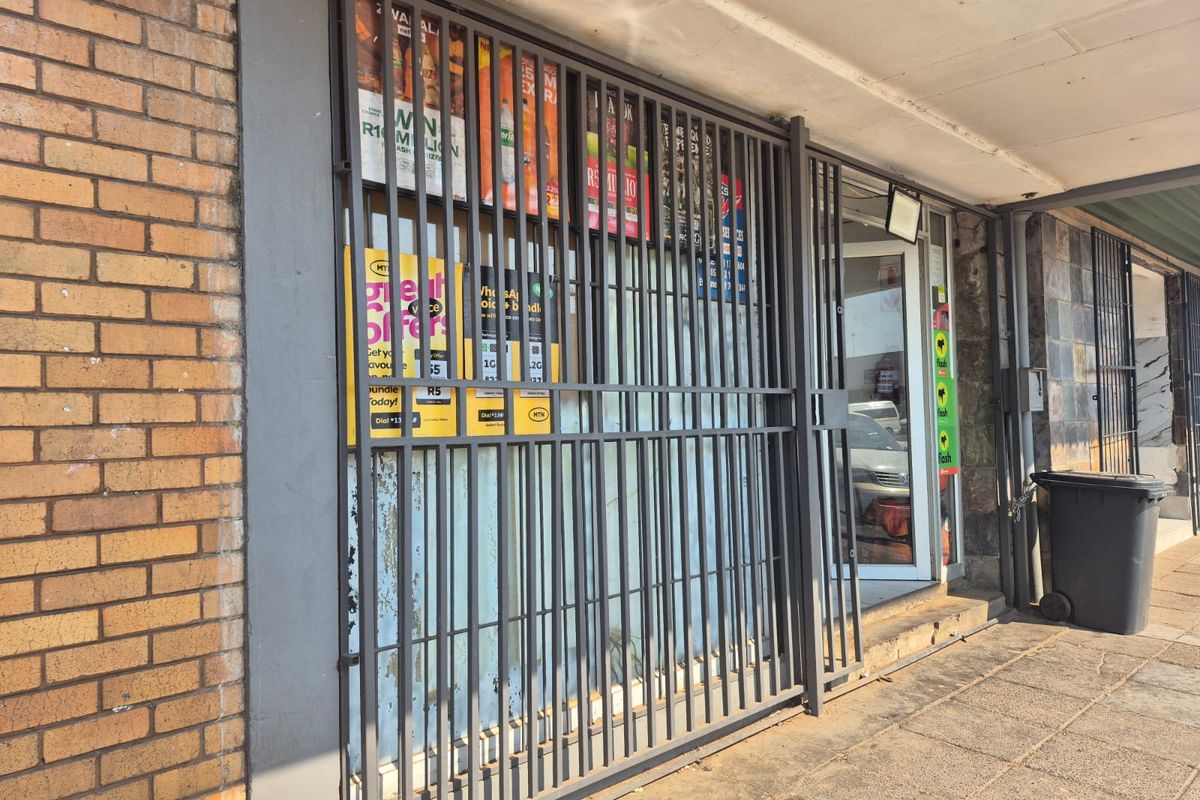 Commercial storefront entrance featuring a security gate, brick facade, and covered walkway area.