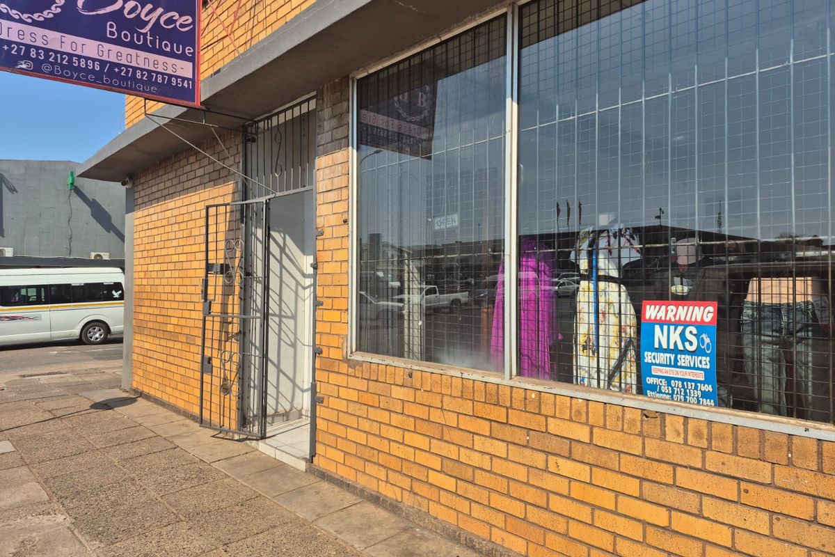 Commercial storefront featuring a face brick facade, large display window with security grille, and a secure entrance gate.