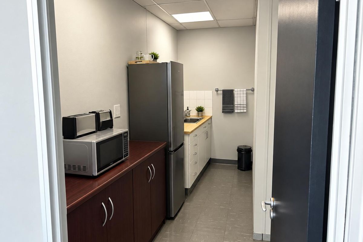A functional office kitchenette featuring built-in cabinetry, laminate countertops, a stainless steel sink, and durable vinyl flooring.