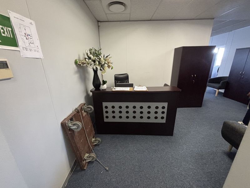 A functional office space featuring a reception desk, carpeted flooring, and a suspended ceiling with recessed lighting.