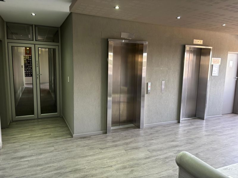 Modern office building lobby featuring dual stainless steel elevators, glass entrance doors, and contemporary laminate flooring with recessed ceiling lighting.