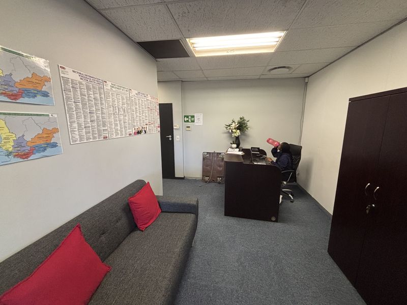 A functional office space featuring a suspended ceiling, carpeted flooring, and built-in storage cabinetry, suitable for professional administrative use.