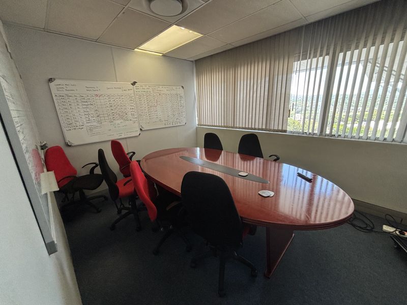 A functional office meeting room featuring a large conference table, wall-mounted whiteboards, and large windows with vertical blinds providing natural light.