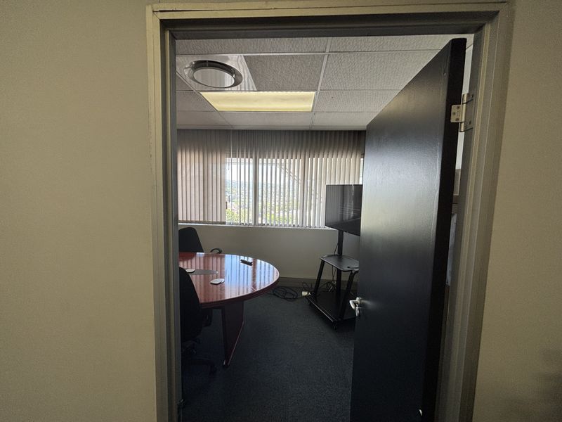 A functional office space featuring a suspended ceiling, recessed lighting, carpeted flooring, and vertical blinds providing natural light.
