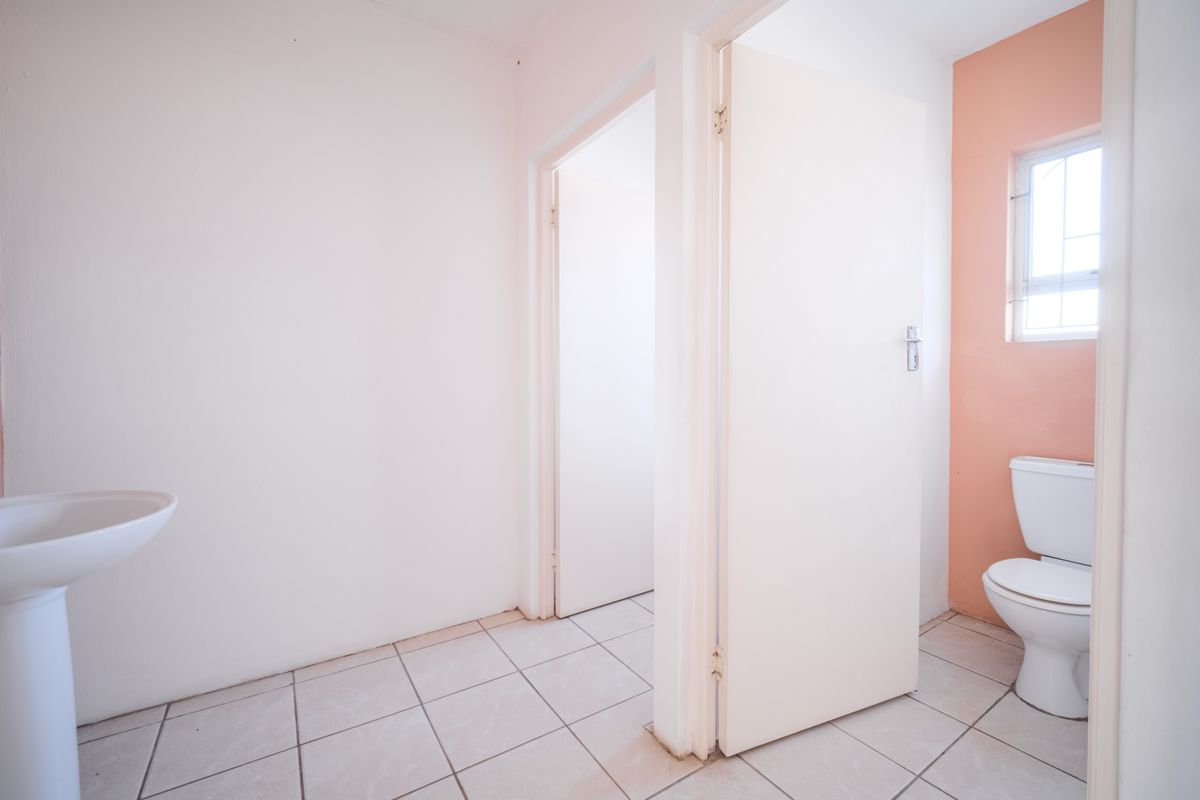 A functional bathroom space featuring a pedestal basin, a standard toilet, and tiled flooring, providing essential facilities for the office environment.