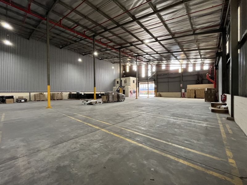Spacious industrial warehouse featuring high ceilings, exposed steel structural beams, fire sprinkler system, and polished concrete flooring with marked loading zones.