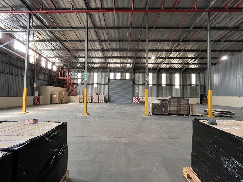 Spacious industrial warehouse featuring high ceilings, exposed steel structural beams, concrete flooring, and a large roller shutter door for efficient loading access.