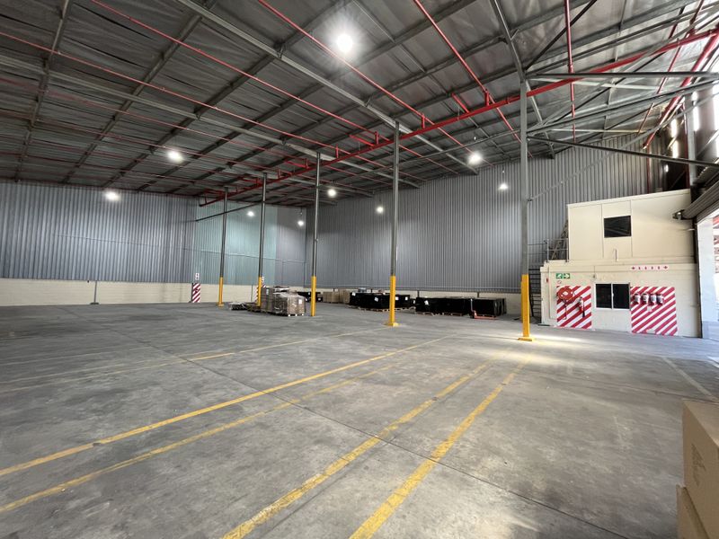 Spacious industrial warehouse featuring high ceilings, exposed steel trusses, fire sprinkler system, concrete flooring, and an integrated office block.