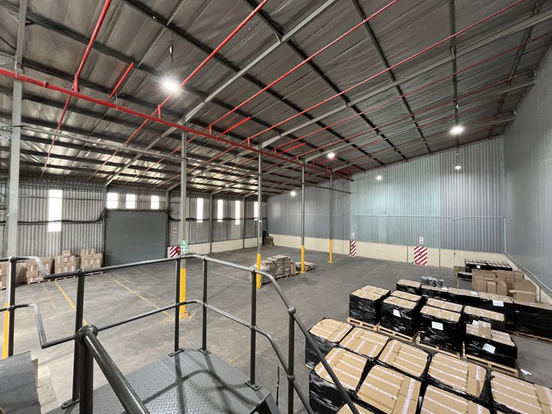 Spacious industrial warehouse featuring high ceilings, exposed fire sprinkler system, metal cladding walls, and a roller shutter door for efficient loading access.