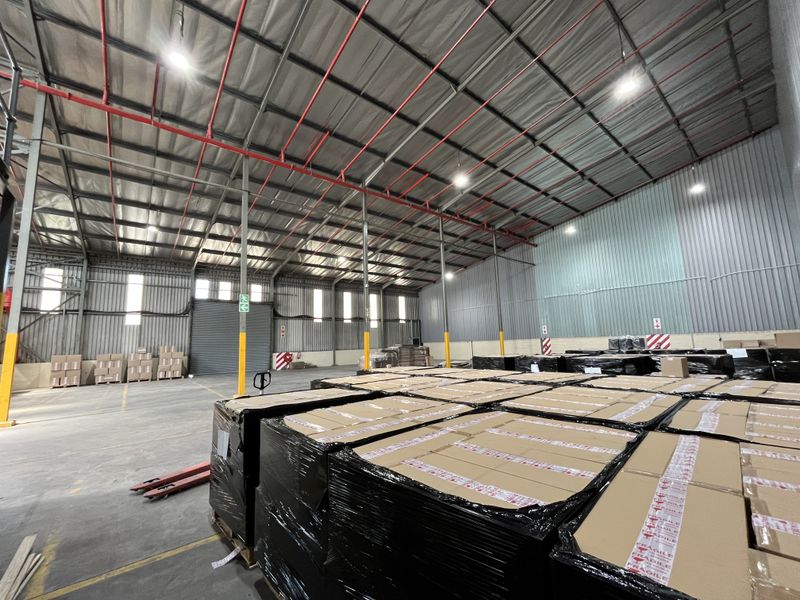 Spacious industrial warehouse featuring high ceilings, exposed steel trusses, fire sprinkler system, and concrete flooring, suitable for storage or manufacturing operations.
