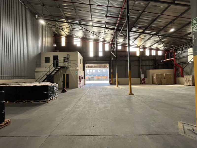 Spacious industrial warehouse featuring high ceilings, exposed steel structure, fire sprinkler system, and an integrated mezzanine office area with staircase access.