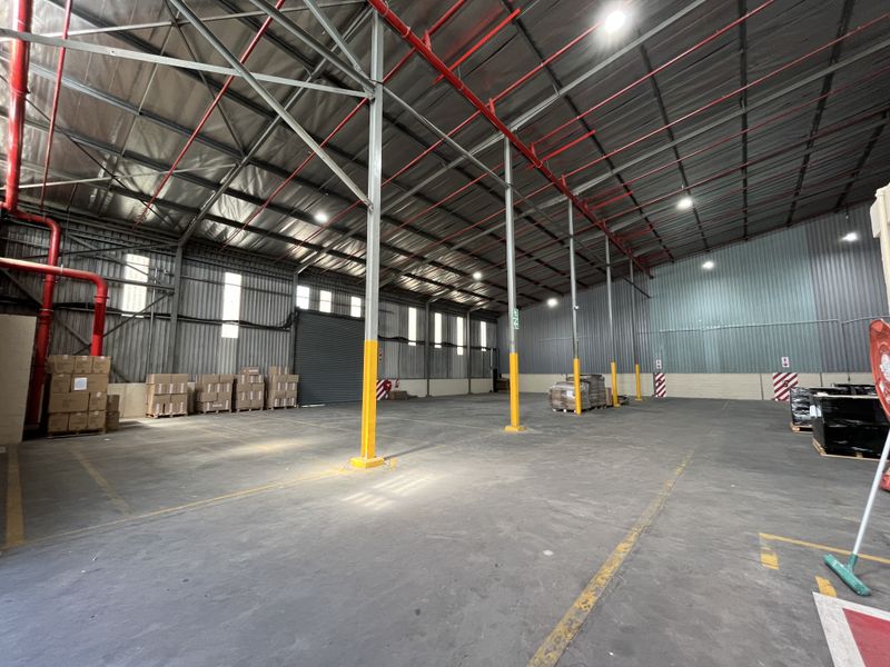 Spacious industrial warehouse featuring high ceilings, exposed steel trusses, fire sprinkler system, concrete flooring, and large roller shutter door access.