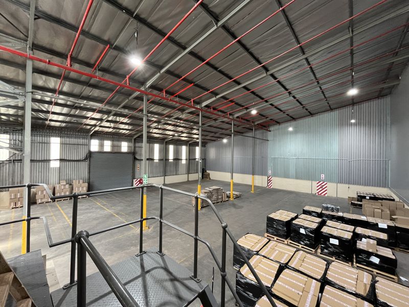Spacious industrial warehouse featuring high ceilings, exposed fire sprinkler system, metal cladding walls, concrete flooring, and a roller shutter door for easy access.
