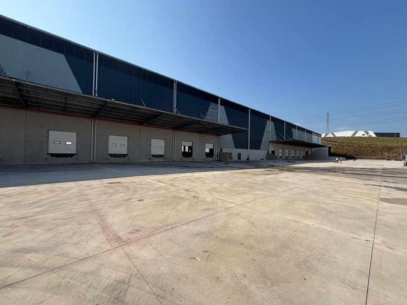 Industrial warehouse exterior featuring multiple loading docks with roller shutter doors, a large concrete yard, and modern metal cladding.