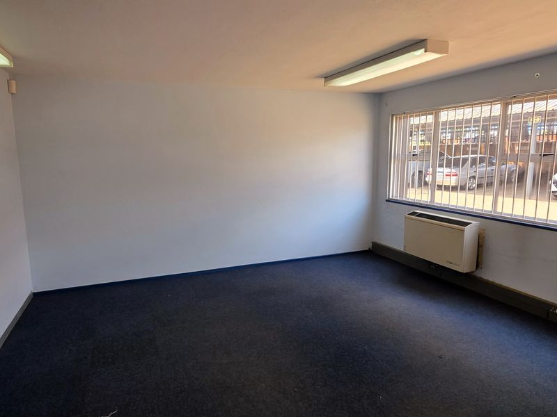 A vacant office space featuring carpeted flooring, wall-mounted air conditioning, and large windows with security bars, suitable for a professional workspace.