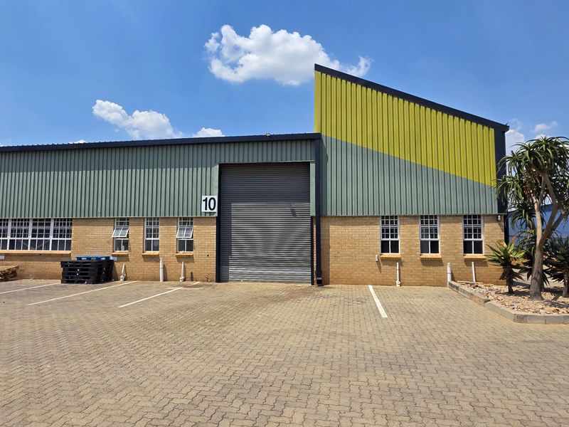 Industrial unit featuring a face brick facade, roller shutter doors, and paved exterior parking area within a secure complex.