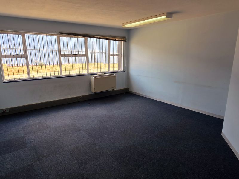An empty office space featuring carpet tiles, a wall-mounted air conditioning unit, and large windows with security bars.