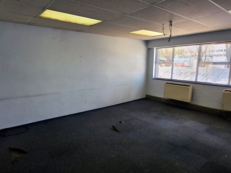 Empty office space featuring suspended ceilings, recessed lighting, large windows, and wall-mounted HVAC units, requiring cosmetic updates to the flooring and wall finishes.