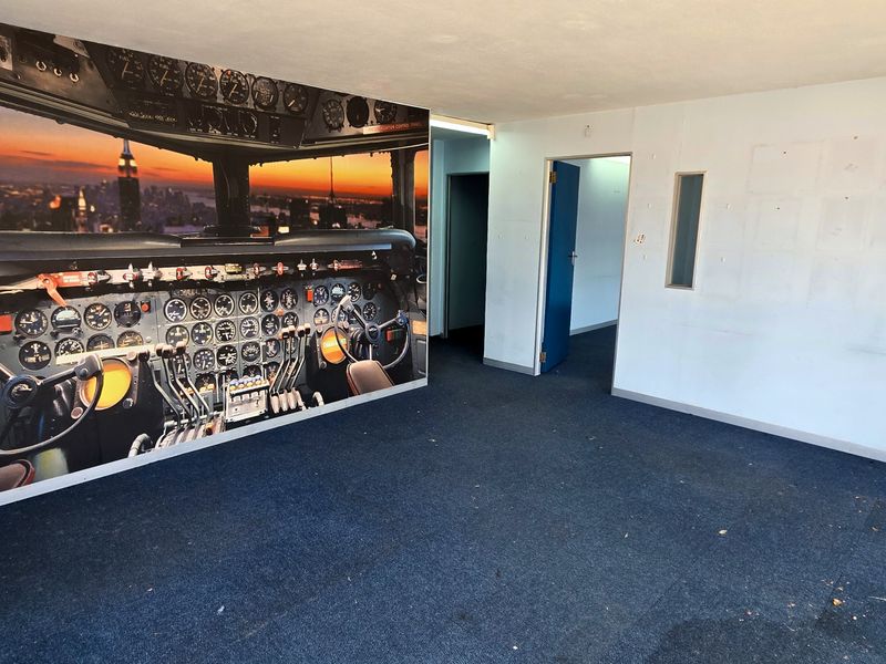 An empty office space featuring blue carpet flooring and a large wall mural, requiring cosmetic updates to the walls and flooring.